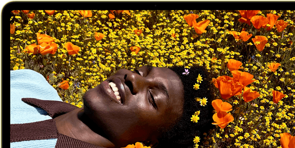 MacBook Neo, citrus colour, screen shows a smiling person lying in a sunny field of flowers