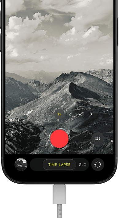iPhone 18 Pro, front exterior, displaying a mountainous landscape, with the camera mode overlay in Time-Lapse mode, with charging cable attached to charging port