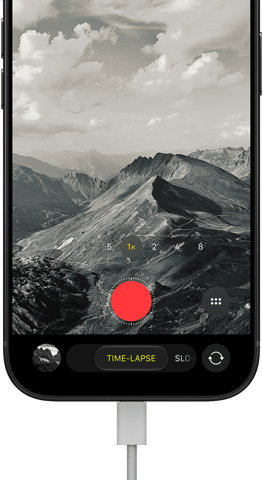 iPhone 18 Pro, front exterior, displaying a mountainous landscape, with the camera mode overlay in Time-Lapse mode, with charging cable attached to charging port